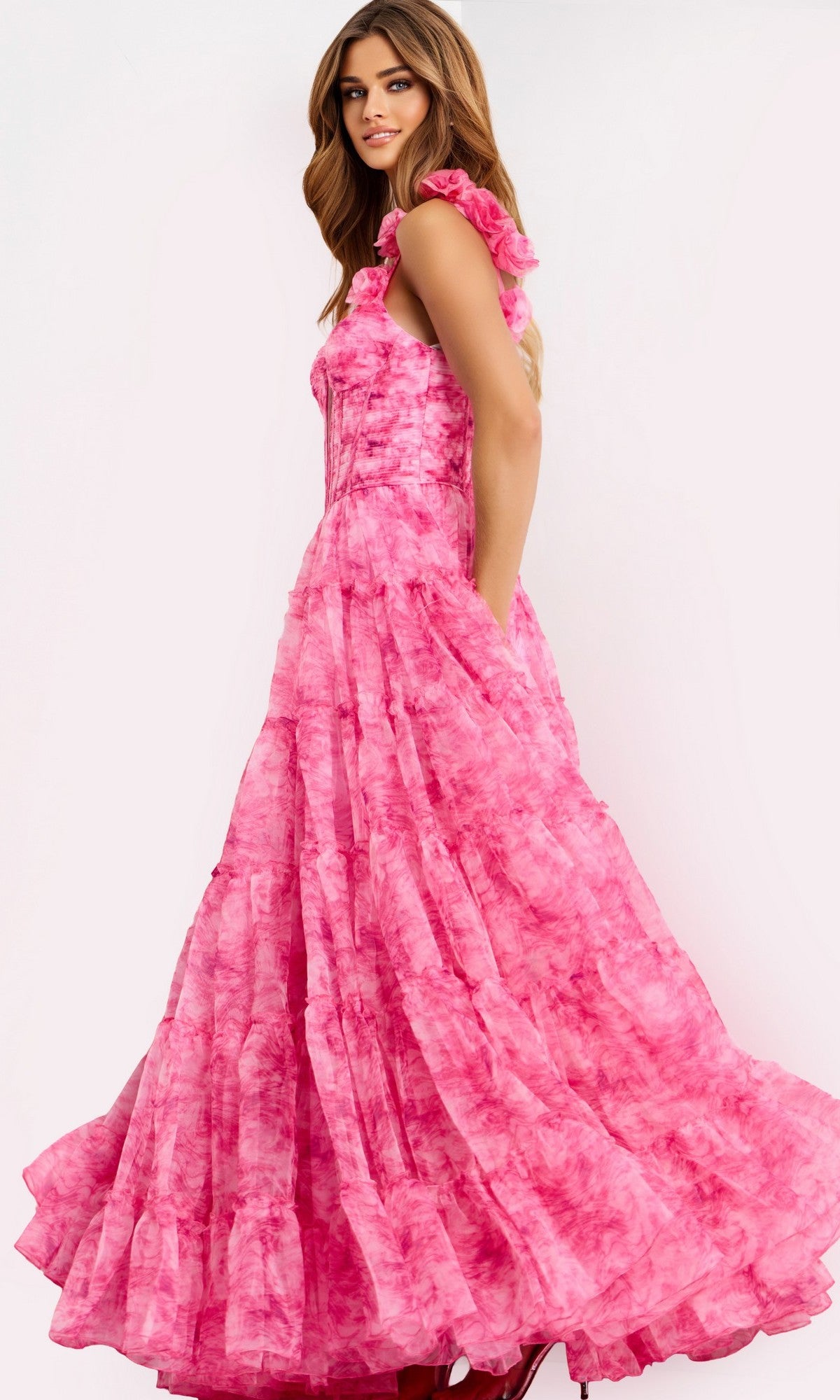A woman wears the Jovani 49074 Long Prom Dress—a floor-length, sleeveless pink gown with a ruffled full skirt and corset-style bodice—standing against a light background.